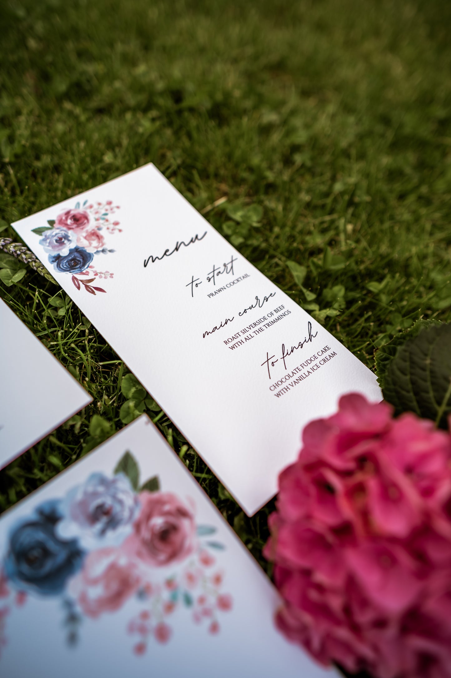 Floral menu cards on grass with pink flowers
